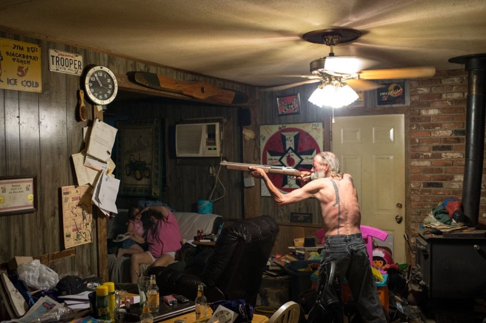 Carl, an Imperial Wizard of a southern-based Ku Klux Klan realm, takes aim with a pellet gun at a large cockroach (on the piece of paper just below the clock) while his wife and goddaughter try to avoid getting struck by a possible ricochet. Photo by Anthony S. Karen